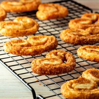 Elephant ear shaped palmier cookies embedded with sugar on a black grid cooling rack.