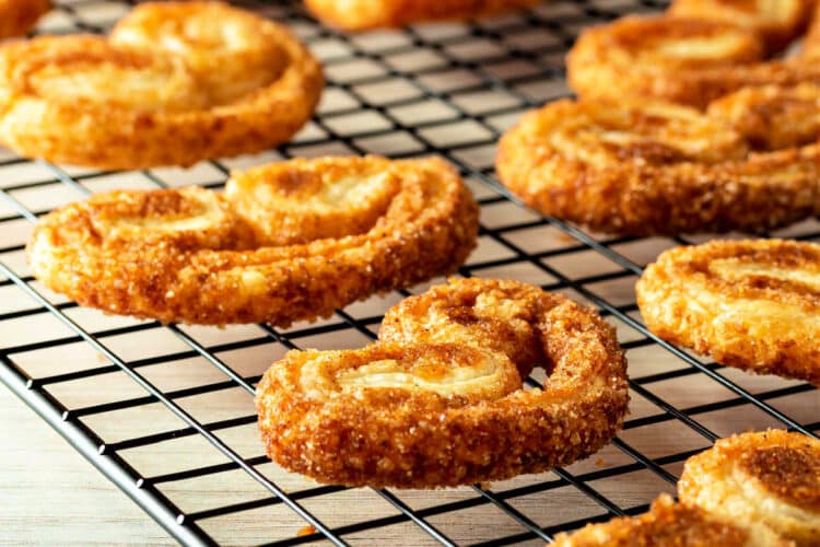 Elephant ear shaped palmier cookies embedded with sugar on a black grid cooling rack.