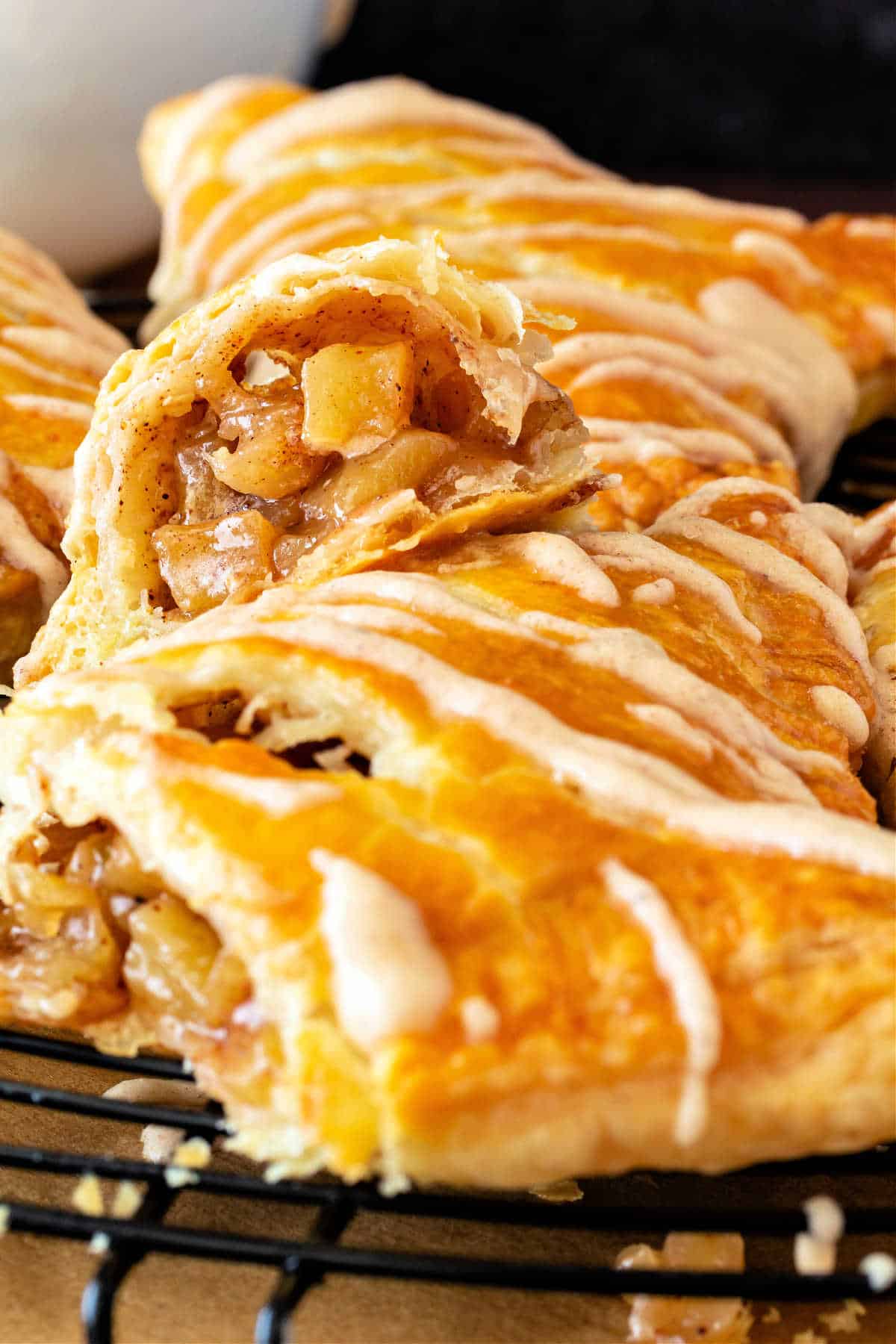 A vertical image of apple turnovers with lines of glaze on them. One is cut open to reveal little chunks of apple.