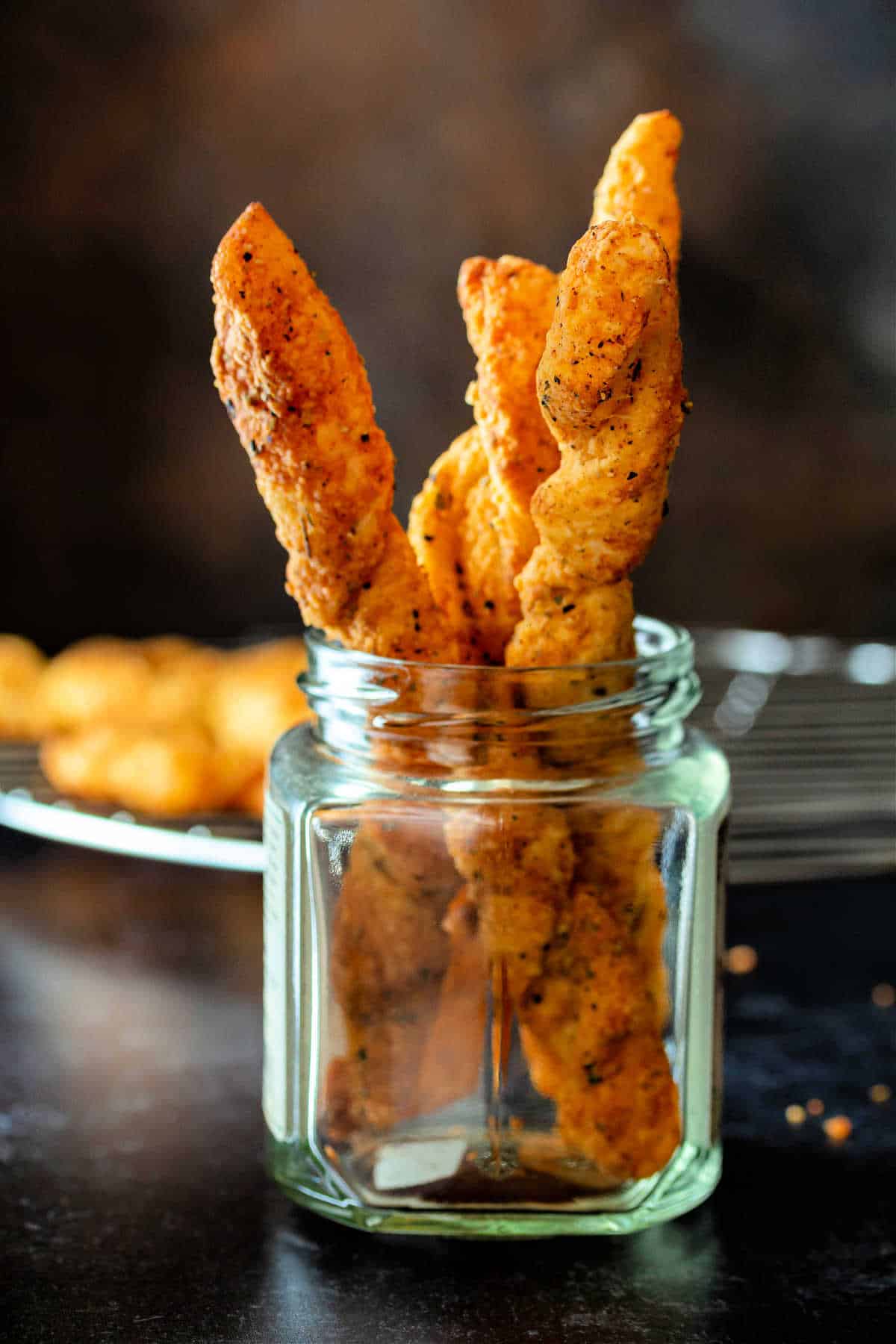 A glass jar with cheese straws in it with more cooling in the background on a metal cooling rack.