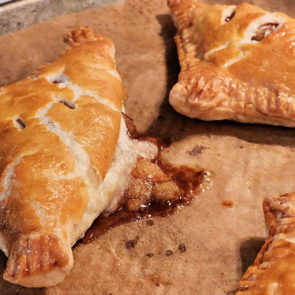 A close up of an apple turnover fresh from the oven. Some of the filling has broken through the crust in the back of the turnover.