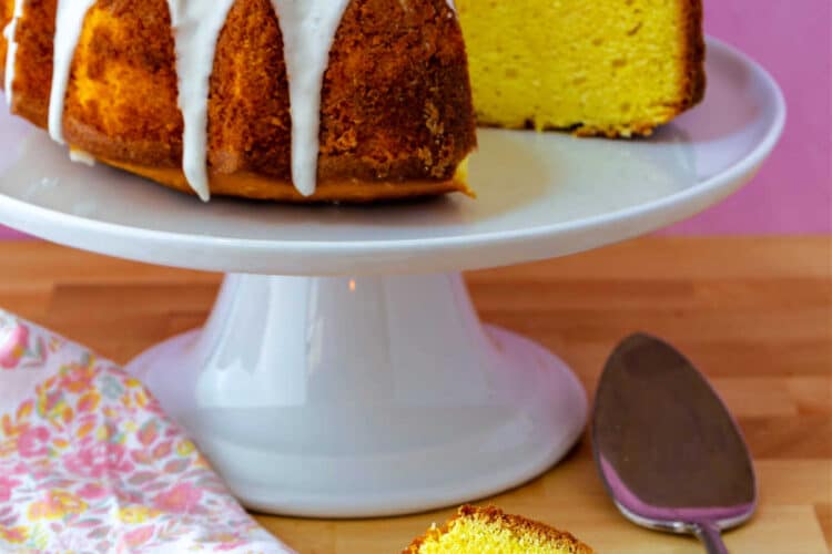 A lemon Bundt cake on a white cake stand with a slice of the cake on a plate.