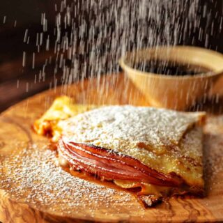 A folded crepe filled with meat and cheese with powdered sugar showering down on top of it.
