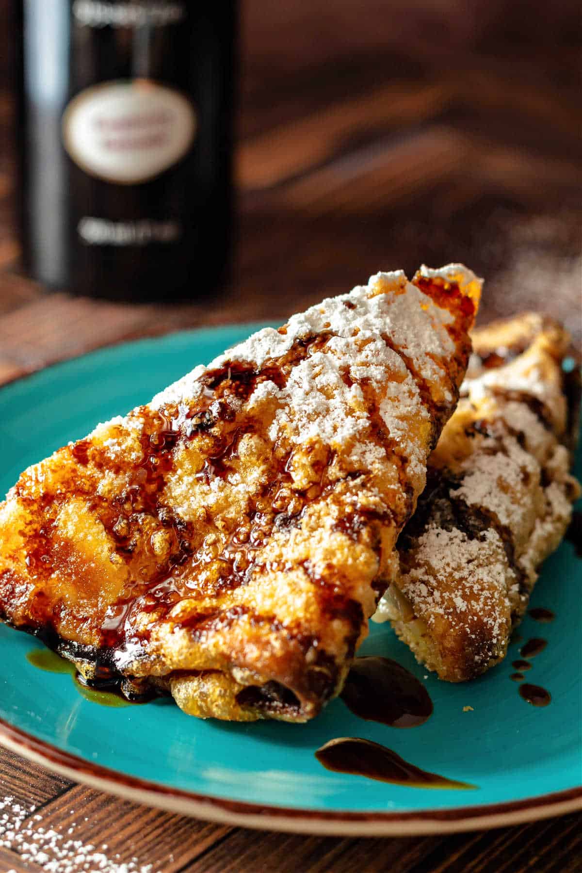 A battered and deep-fried triangle of filled creip drizzled with balsamic vinegar with a dusting of powdered sugar on it.