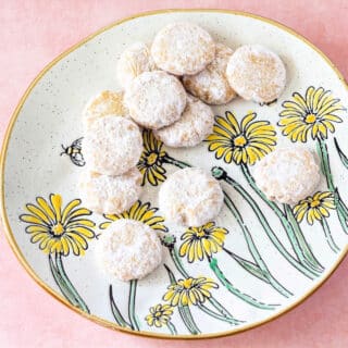 A plate of powdered sugar-coated round cookies. The plate has pictures of daisies on it.