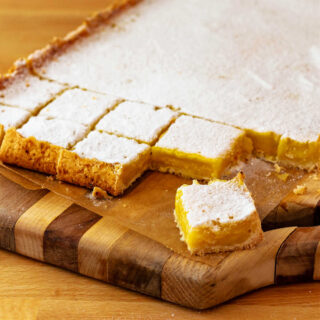A block of lemon bars on a cutting board. Some are cut into small squares.