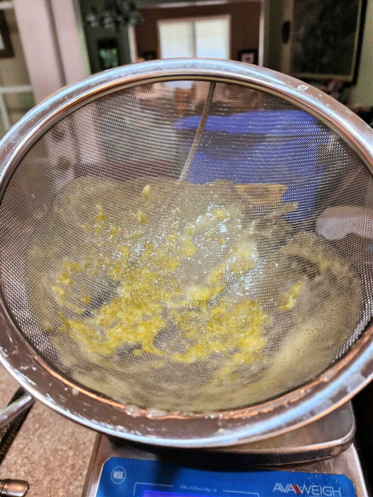 A close-up of the inside of a fine mesh strainer with tiny bits of cooked egg and lemon zest in the bottom.