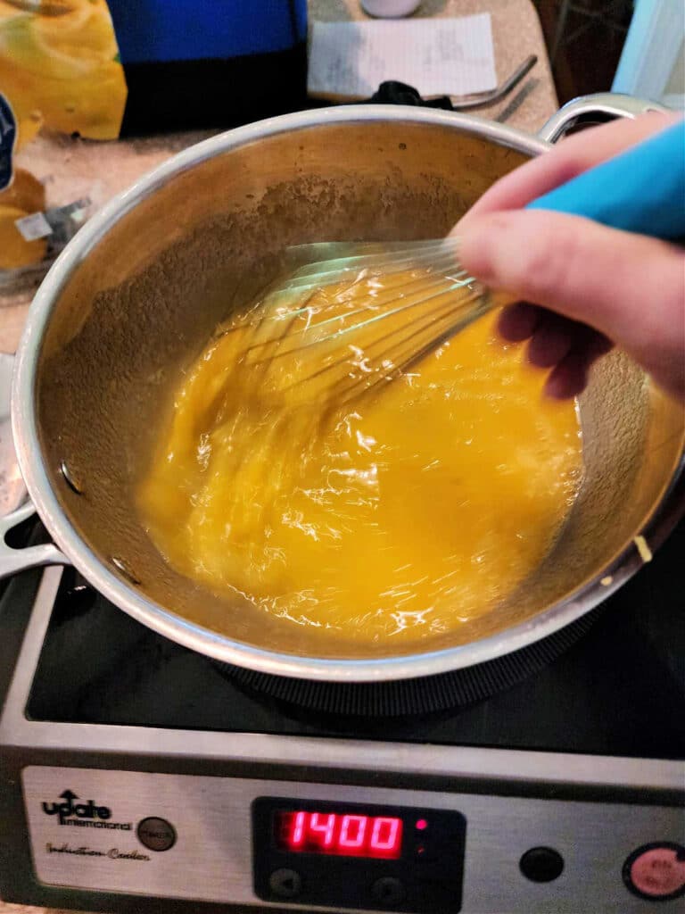 Whisking yellow liquid in a pot on an induction burner.