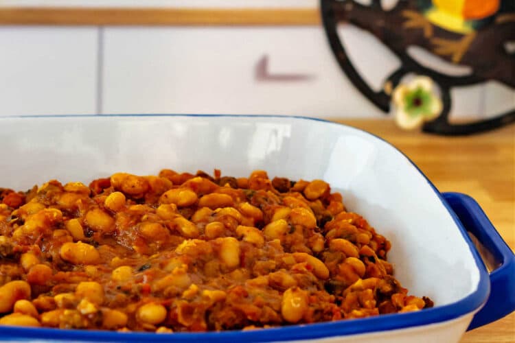 A white pottery baking dish with a blue rim and blue handles with chorizo baked beans in it.
