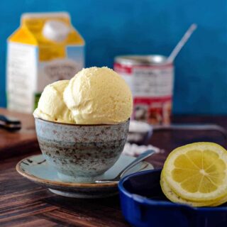 A small bowl with scoops of ice cream in it plus lemon slices, heavy cream, and sweetened condensed milk in the background.