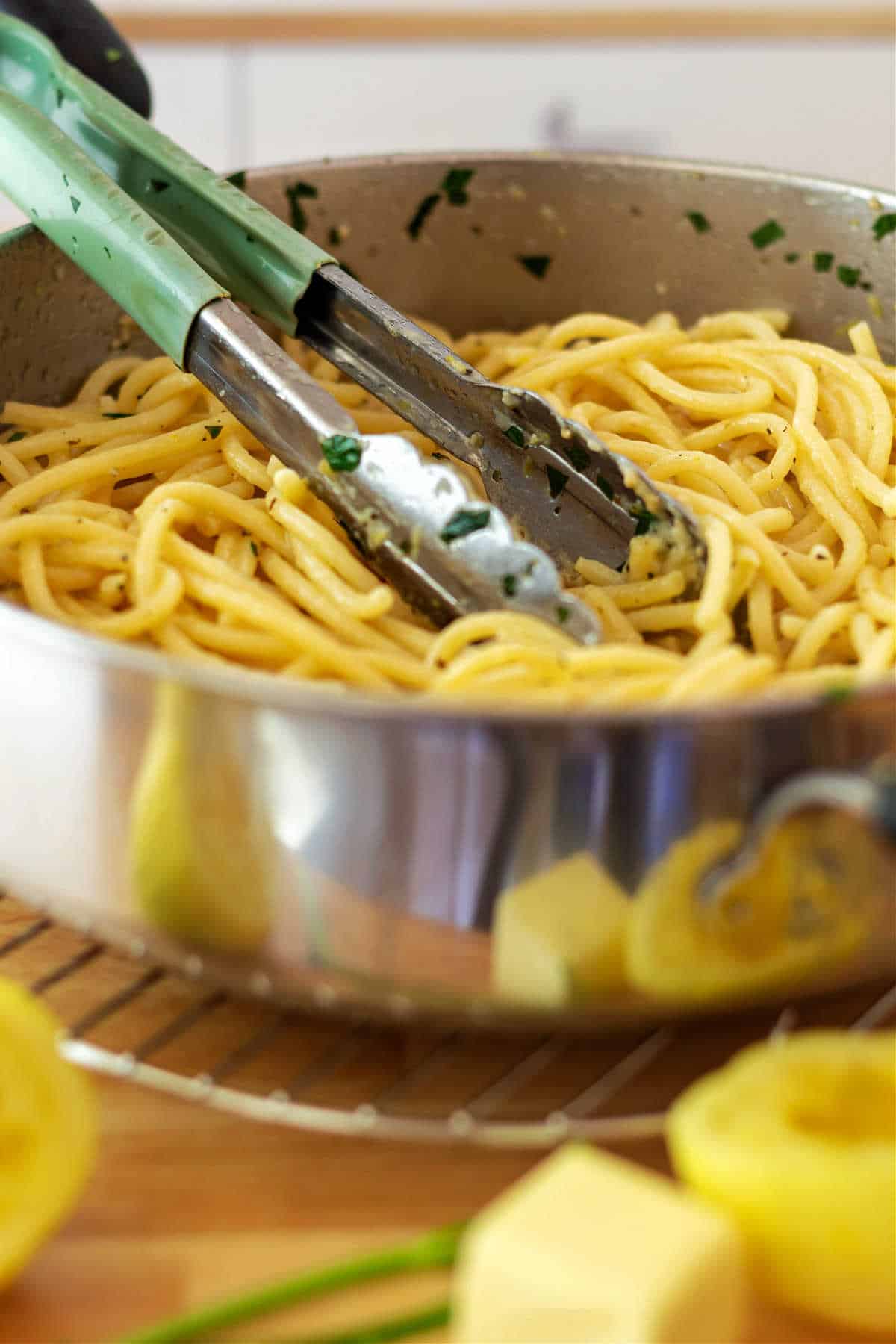 A saute pan full of long, thick pasta with tongs in it and lemons and some butter in front.