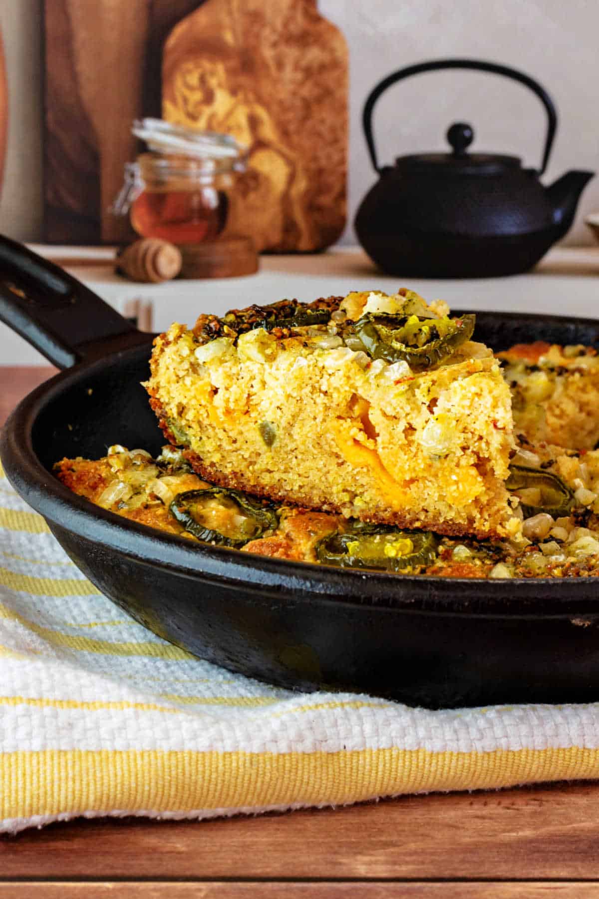 A slice of jalapeno cheddar cornbread on top of the rest of the cornbread in a cast iron skillet.