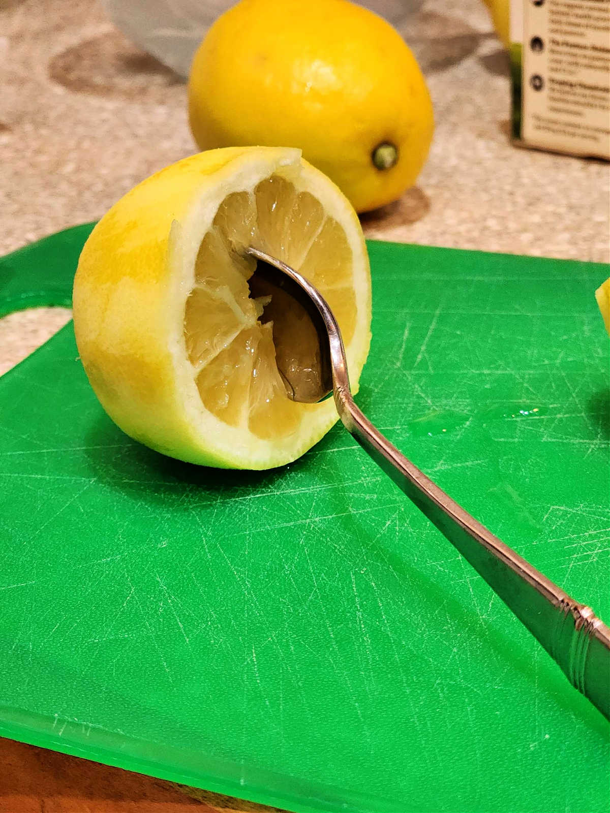 Half a lemon on a green cutting board with the bowl of a spoon inserted in the center.