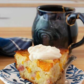 A slice of peach breakfast cake topped with vanilla yogurt with a cup of coffee.