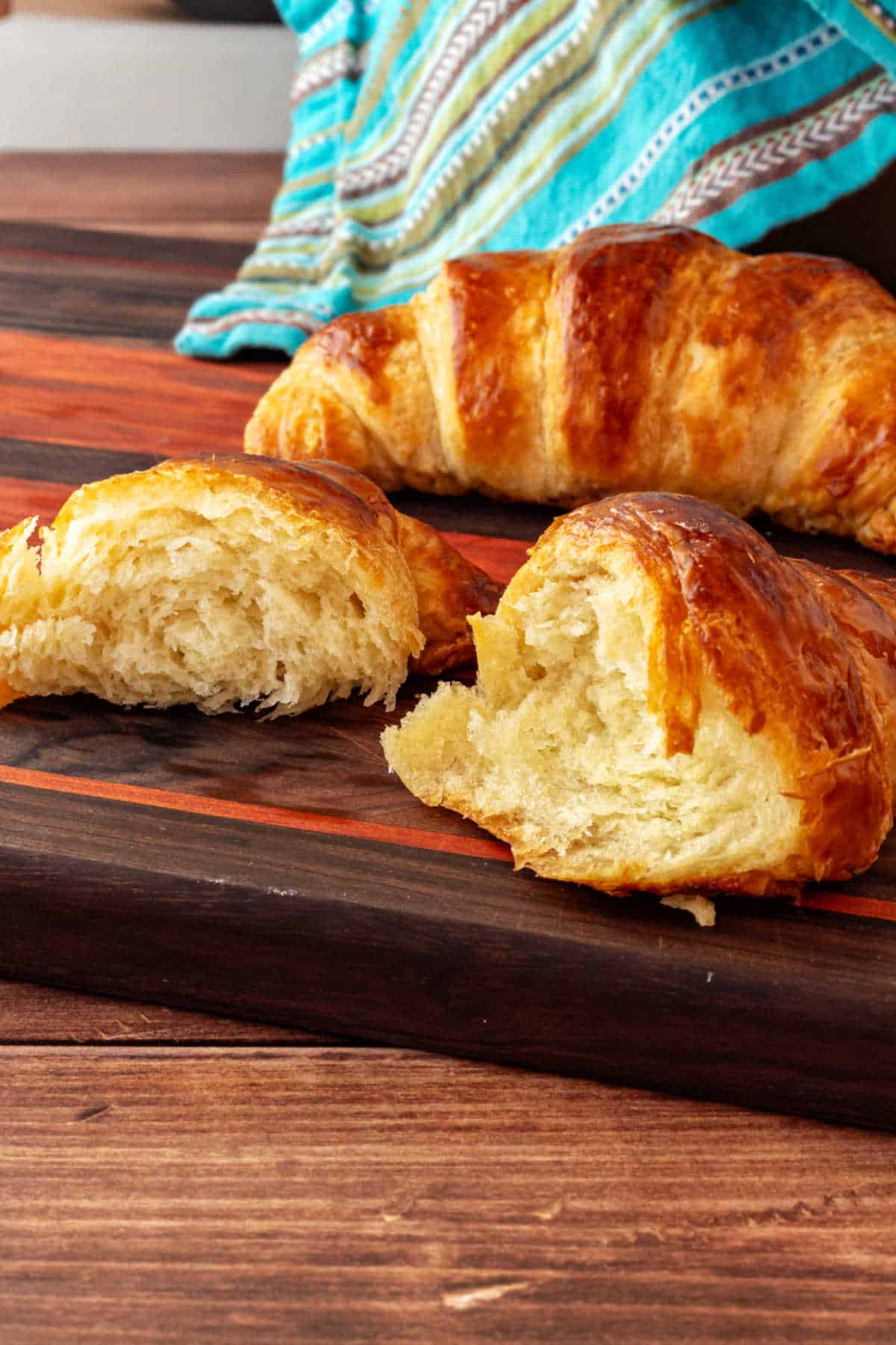 A croissant that has been pulled in half on a cutting board with a full croissant behind it.