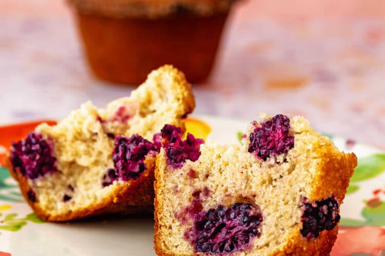 A large muffin split in half to show it filled with large, purple blackberries.