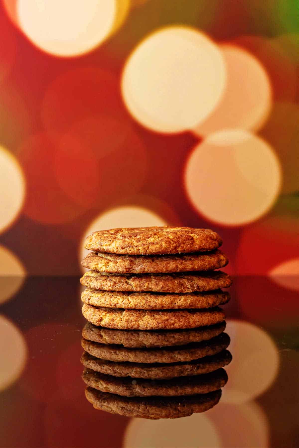 A stack of cookies shot on a dark, reflective surface with Christmas lights in the background and reflecting off the surface.