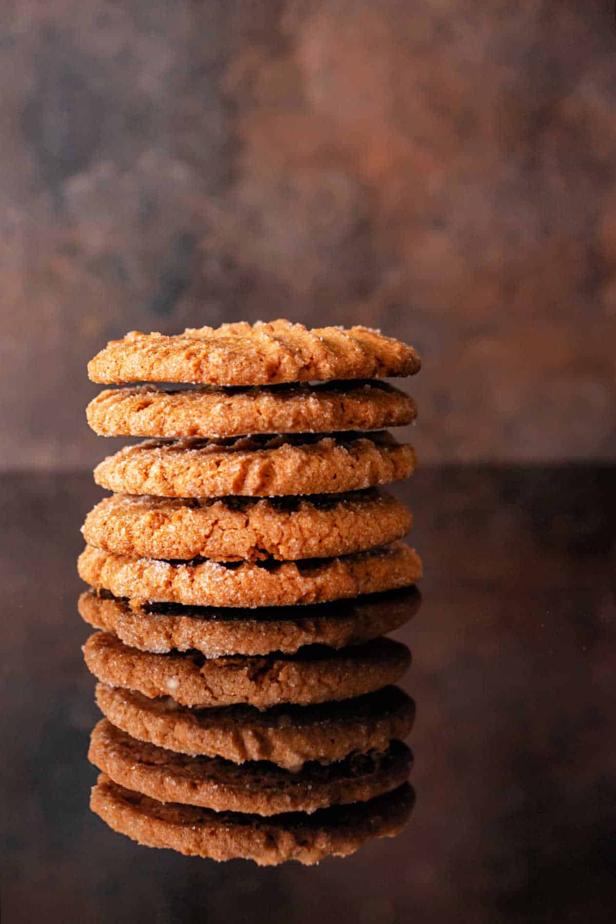 A stack of 5 large peanut butter cookies on a dark, reflective surface.