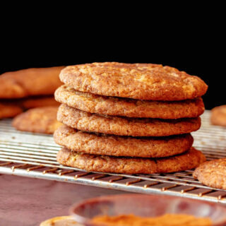 A stack of 5 snickerdoodles on a rack with a small bowl of cinnamon in the foreground.