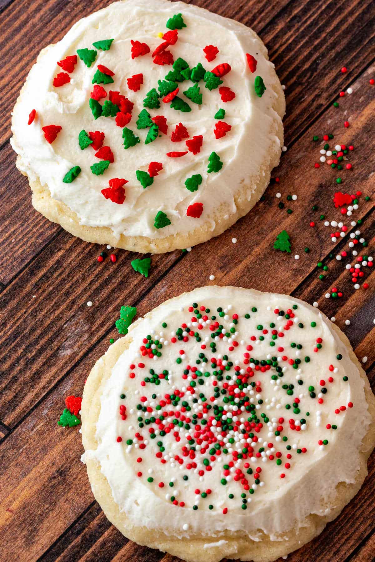 A close up of two round sugar cookies, iced with white frosting and decorated with red and green sprinkles for Christmas.