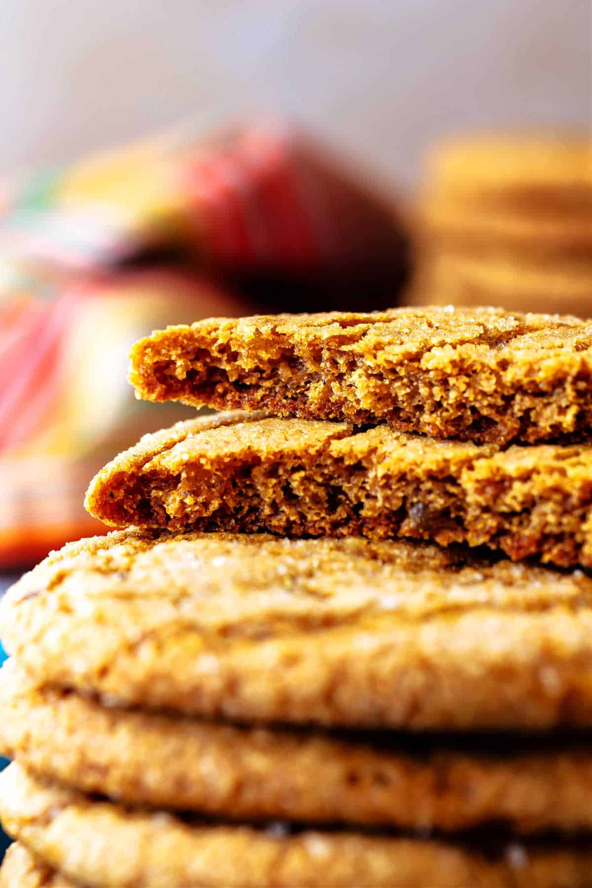 A close up of a stack of gingersnaps with the top one broken in two. The two halves rest on top of each other to show the dense, moist, chewy interior.