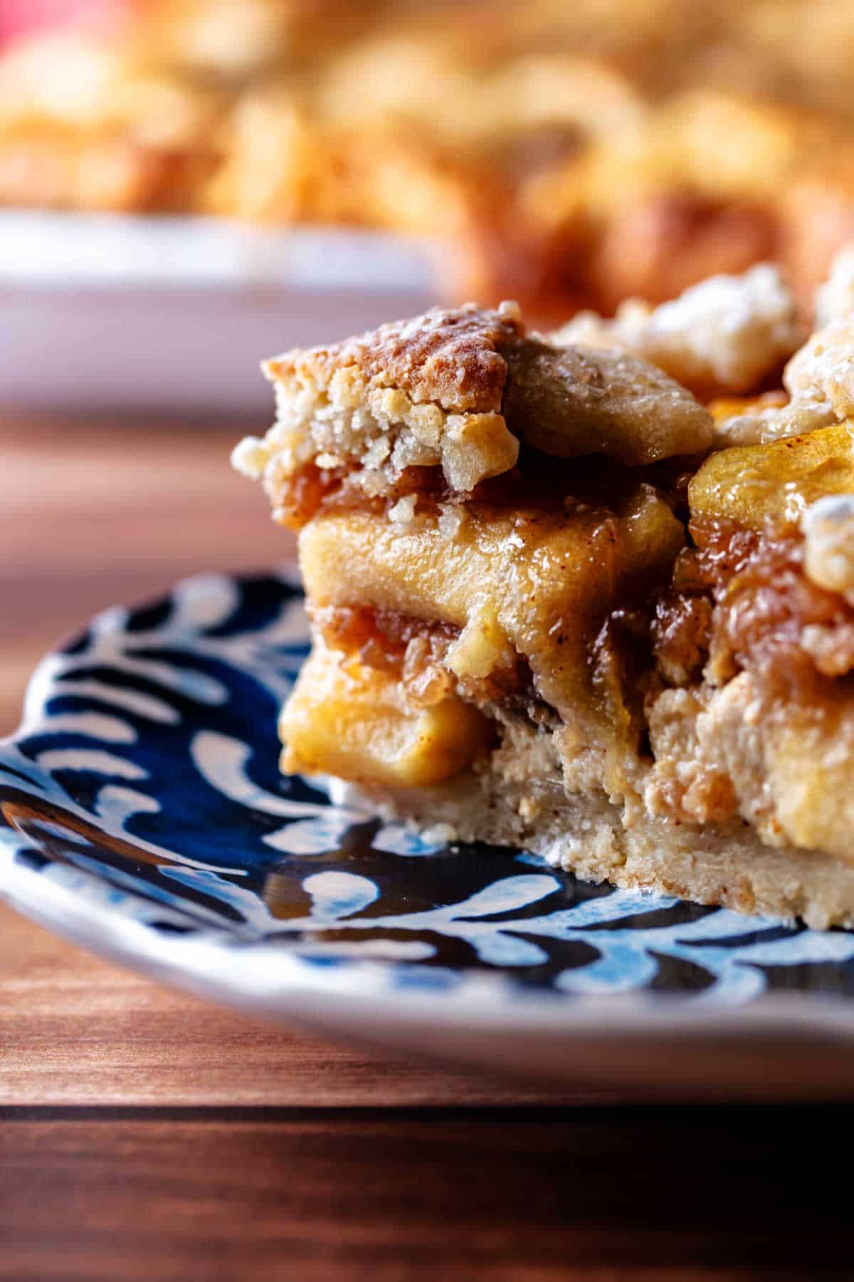 A close-up shot of a slice of apple custard pie showing the cookie crust, custard layer, and the brown-sugar apples.