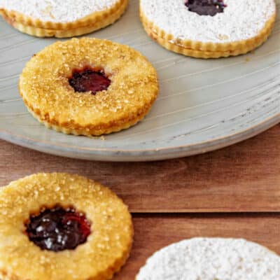 Five Linzer cookies, three dusted with powdered sugar and two with coarse sugar.