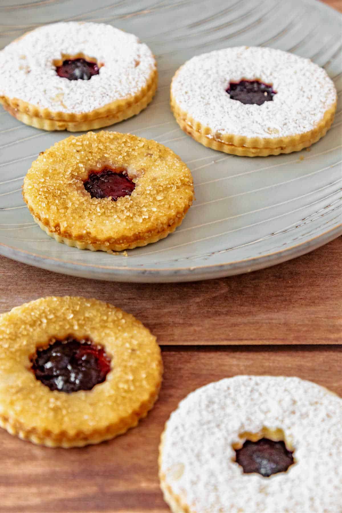 Five Linzer cookies, three dusted with powdered sugar and two with coarse sugar.