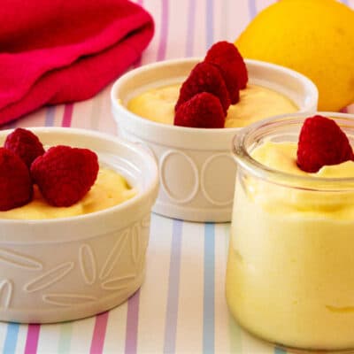 Two white ramekins and one small glass jar of lemon mousse all topped with raspberries.