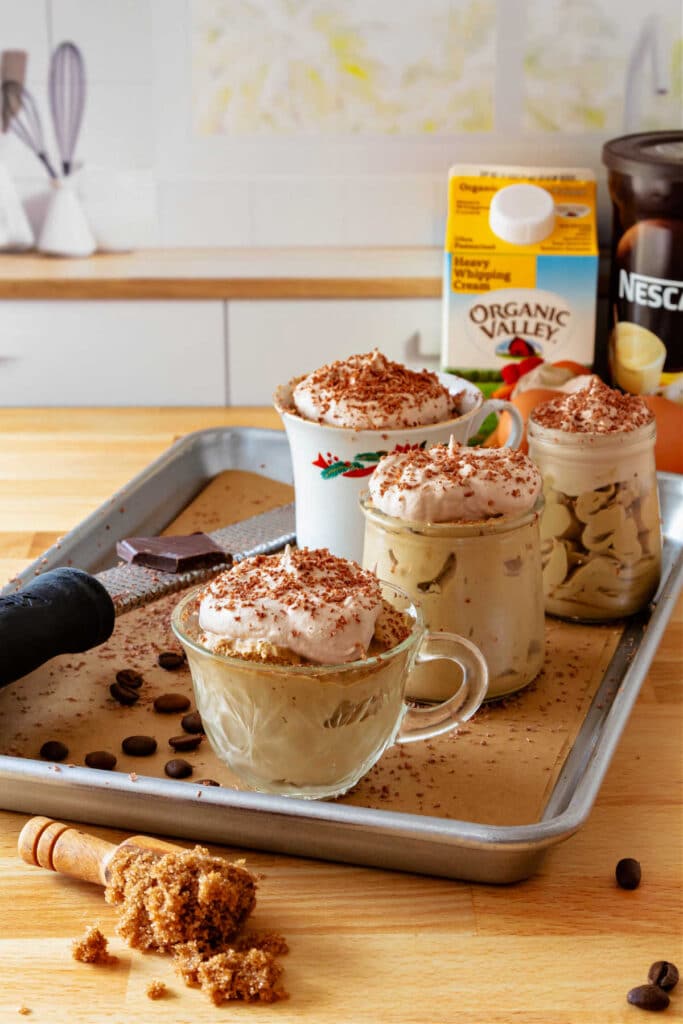 A tray of four containers of coffee mousse with a carton of heavy cream and a can of instant coffee in the background.
