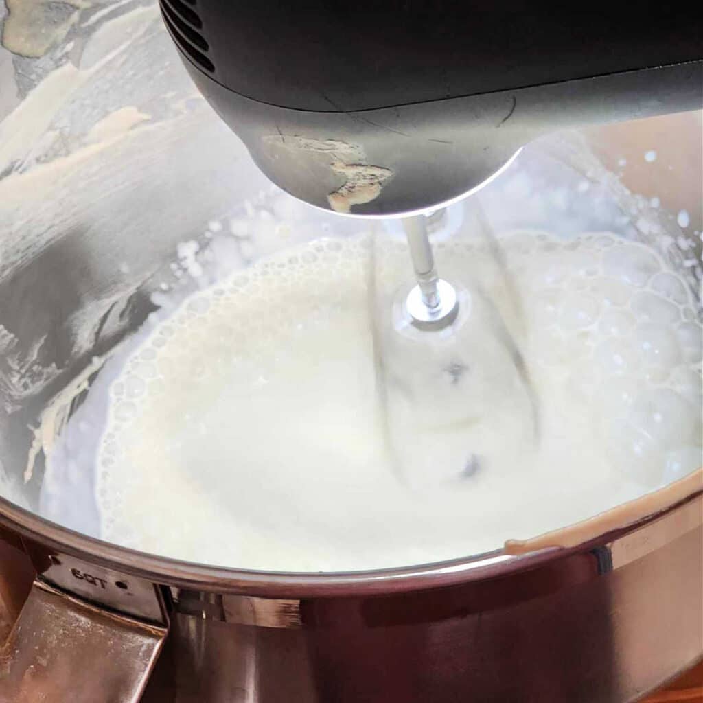 Using a hand mixer to whip cream in a metal bowl.