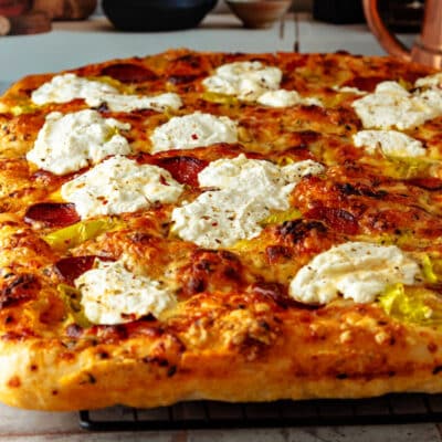 A square image of a grandma pizza topped with spoonfuls of ricotta cheese.