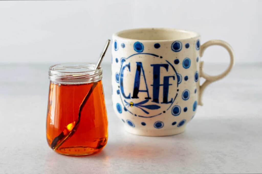 A horizontal image of a glass jar of caramel syrup and a coffee mug.