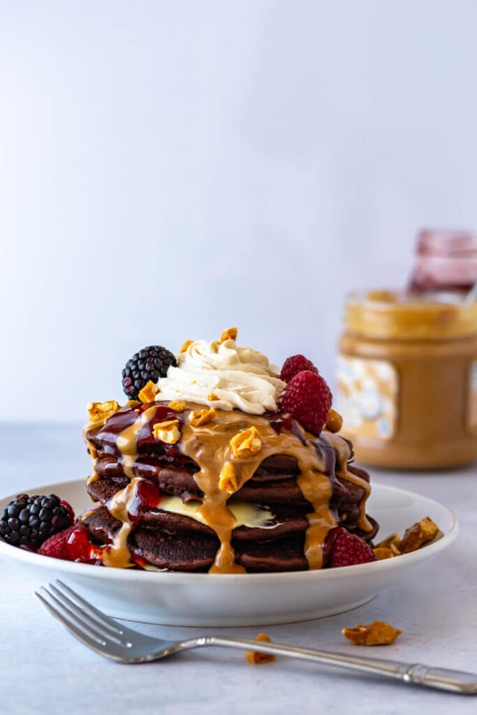 A stack of chocolate pancakes with strawberry and peanut butter sauces poured over the top.