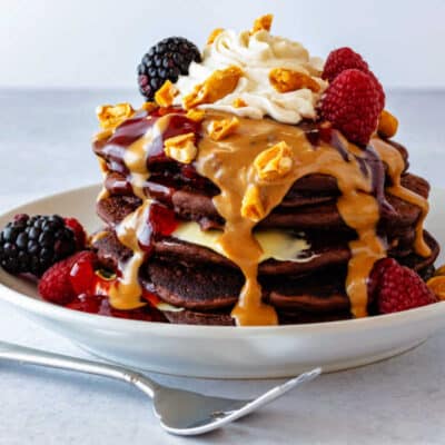 A stack of pancakes with peanut butter and jelly syrups pouring down the sides.