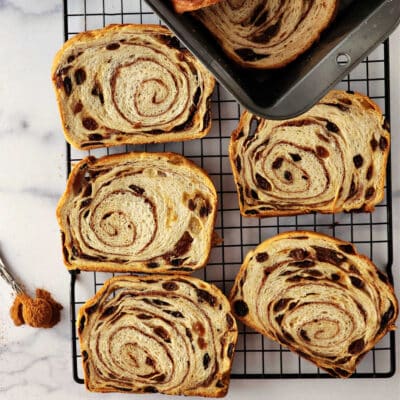 An overhead shot of 5 slices of cinnamon raisin swirl bread on a cooling rack with a teaspoon of cinnamon off to the left side.