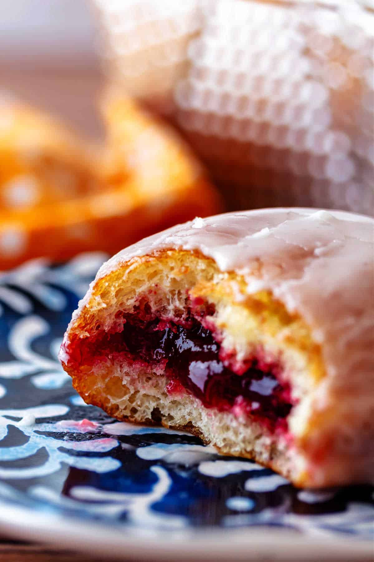 A close-up image of a jelly donut with a couple of bites taken out of it to reveal the ruby red raspberry filling.