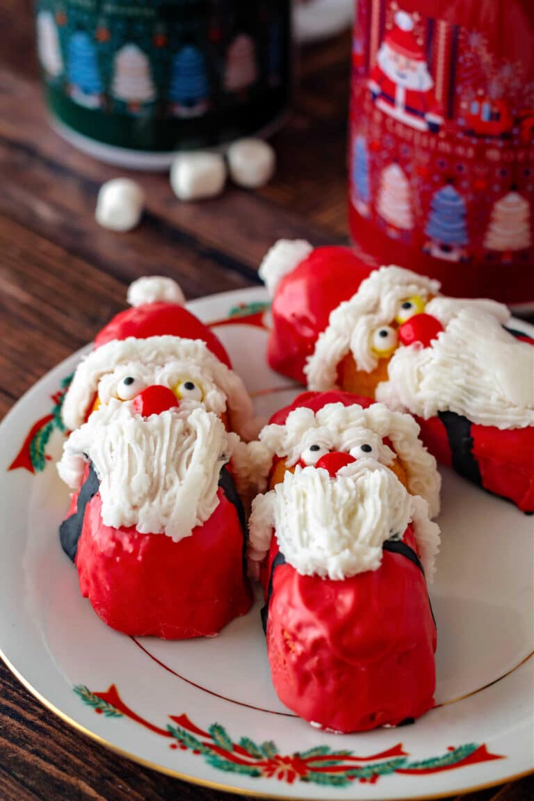 Three Twinkies decorated to look like Santa Clauses on a white plate with a holly and red bow border.