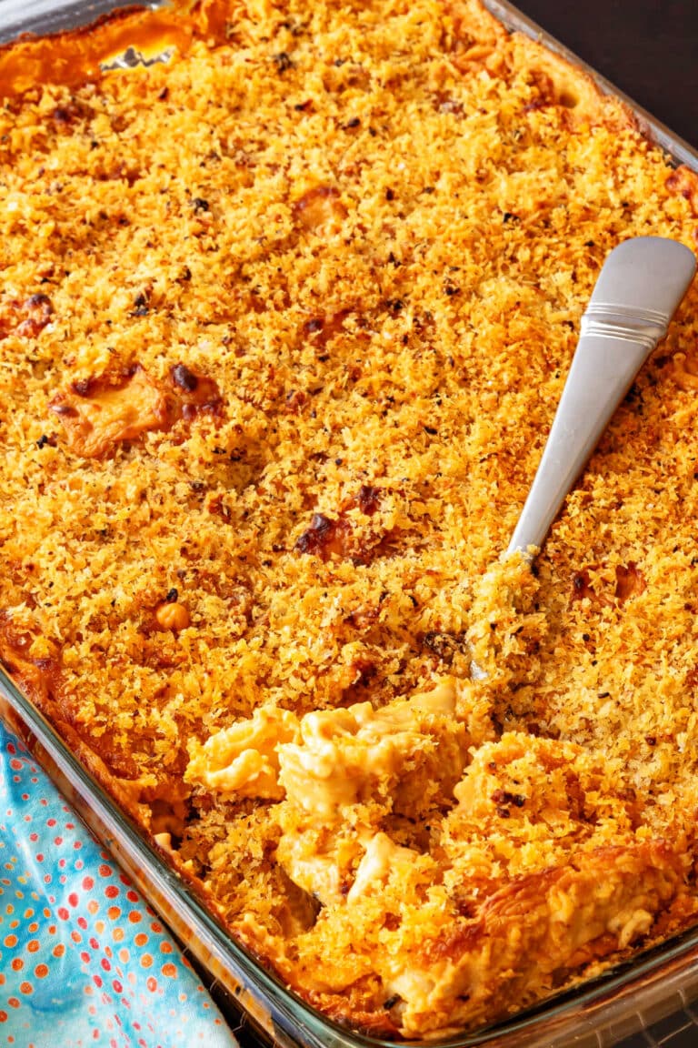 A high-angle shot of a rectangular casserole dish full of panko-topped baked shells and cheese with a spoon in it.