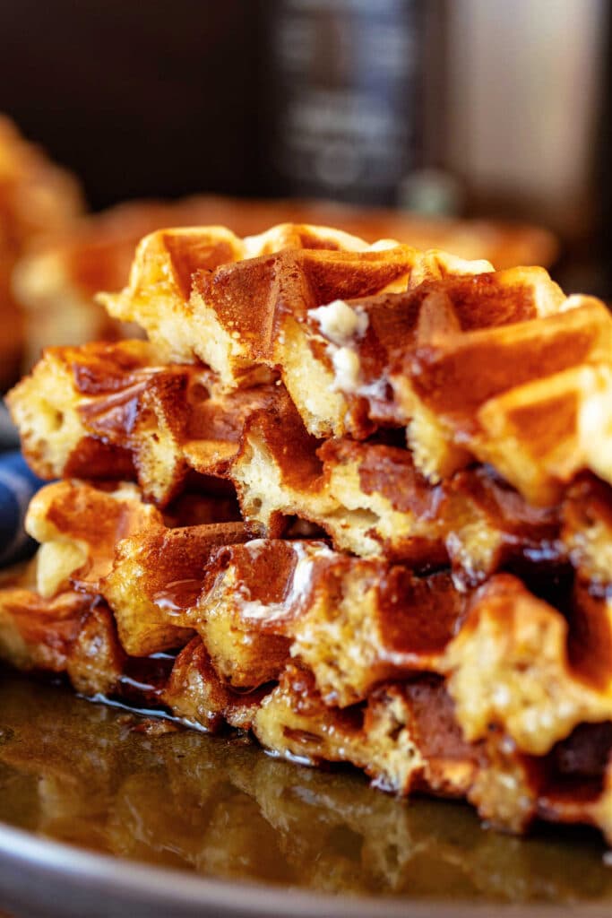 Overnight malted yeast waffles with crisp golden edges, fluffy interiors, and maple syrup soaking into the torn waffle pieces.