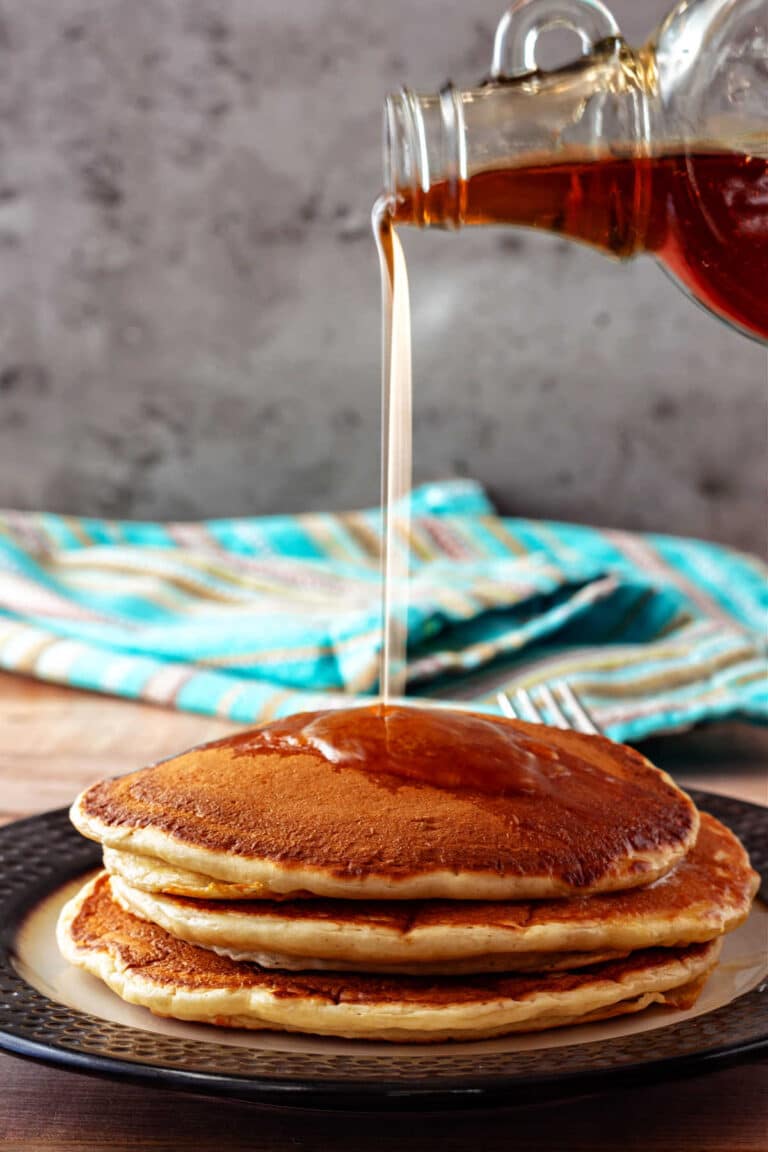 A stack of 3 pancakes with syrup pouring over them.