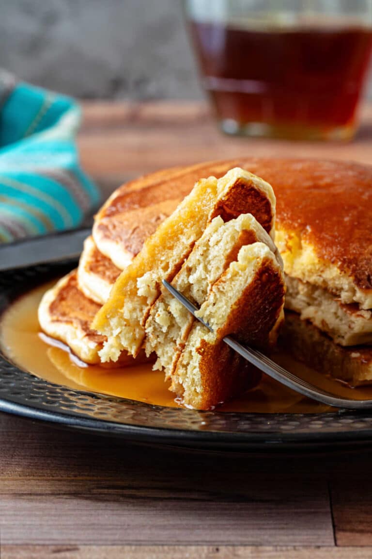 Overnight yeast pancakes with fluffy interiors, crisp golden edges, and maple syrup on a black plate.