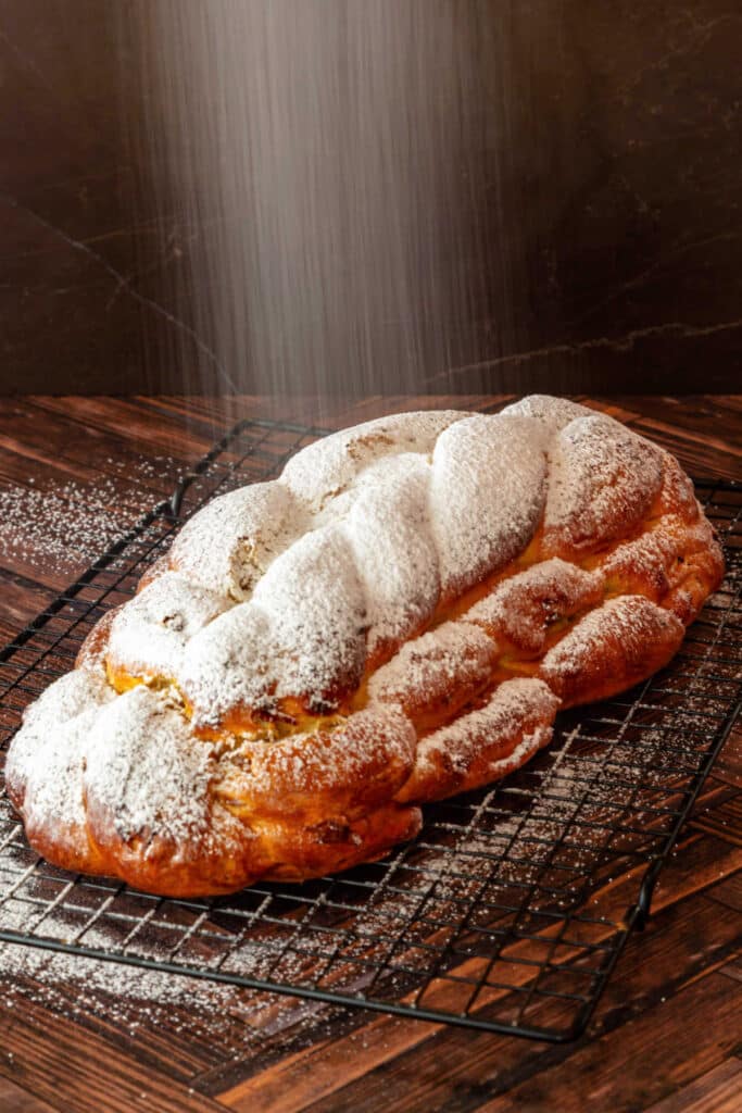 A braided sweet bread on a black cooking rack with powdered sugar showing down over the top.