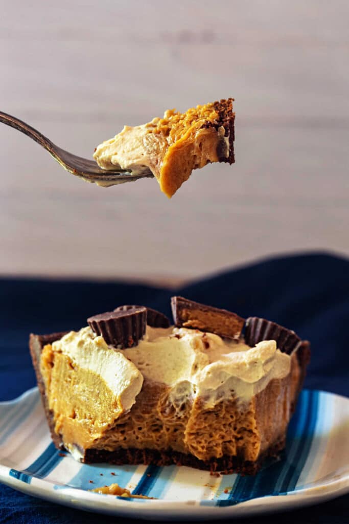 A partially eaten slice of peanut butter cloud pie showing airy filling and chocolate crust, with a bite on a fork above it.