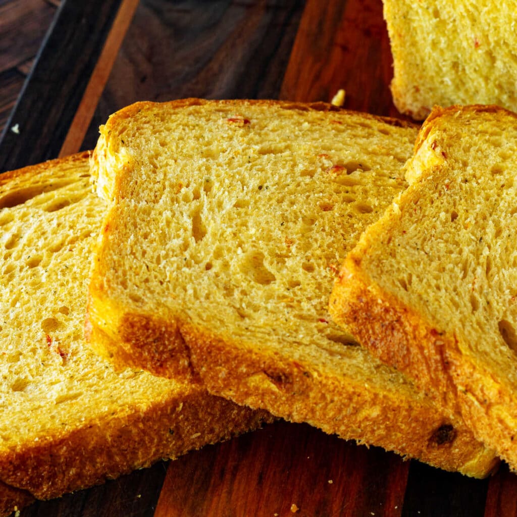 A close-up image of sliced bread fanned out on a cutting board to show the even crumb and little bits of sun-dried tomato in the loaf.
