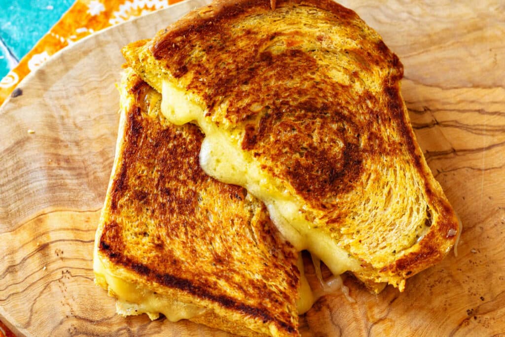 A golden-brown grilled cheese with melty, oozing cheese, sliced and overlapped.
