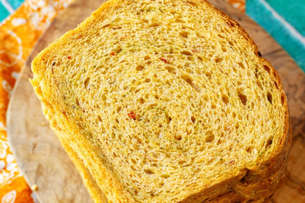 A close-up shot of a pale orange slice of sandwich bread with a subtle swirl of green pesto running throughout. The slice shows full integration and no delamination.