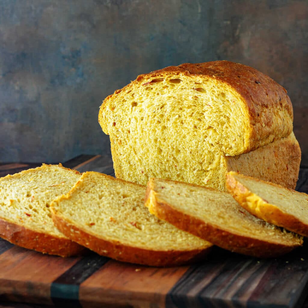 A cut loaf of tomato basil sandwich bread with several slices fanned out on a cutting board.