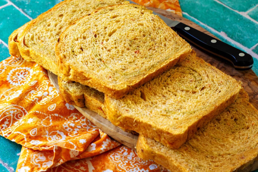 Several slices of bread with a subtle pesto swirl arranged on a cutting board. The crumb is even and perfect for sandwiches.