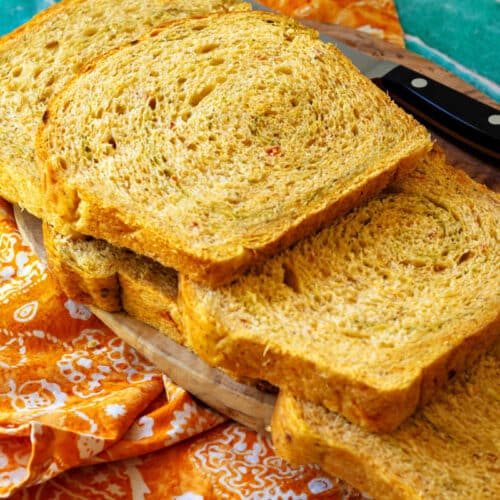 Several slices of bread with a subtle pesto swirl arranged on a cutting board. The crumb is even and perfect for sandwiches.